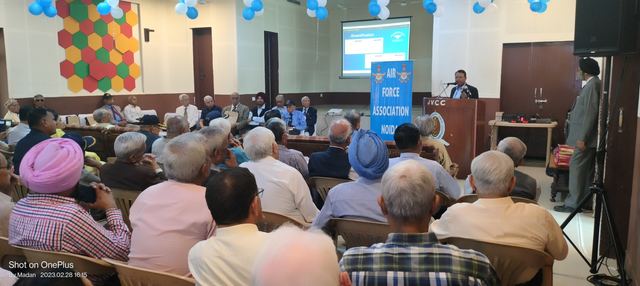 Veterans and family members seated in a hall facing a presentation screen, with an Air Force Association Noida Branch banner beside the stage