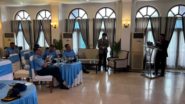 Speaker at a lectern addressing officers seated across a bright hall