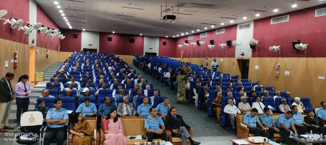 Auditorium filled with Air Force personnel in uniform and civilian guests seated in blue rows
