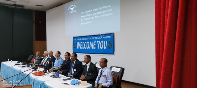 Panel seated at a draped dais in front of a screen and an Air Force Association UP Branch Kanpur welcome banner