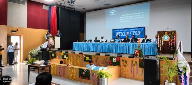 Decorated auditorium stage with a long dais, floral arrangements and a projection screen