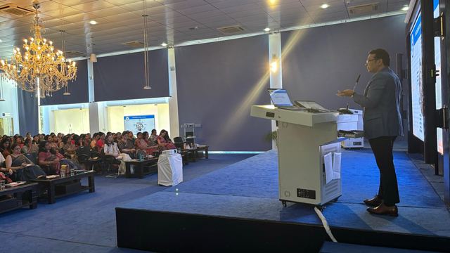 Speaker at a lectern on a raised stage addressing a large seated audience