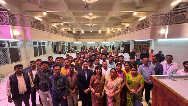 Large group of attendees standing together for a photograph inside a community hall